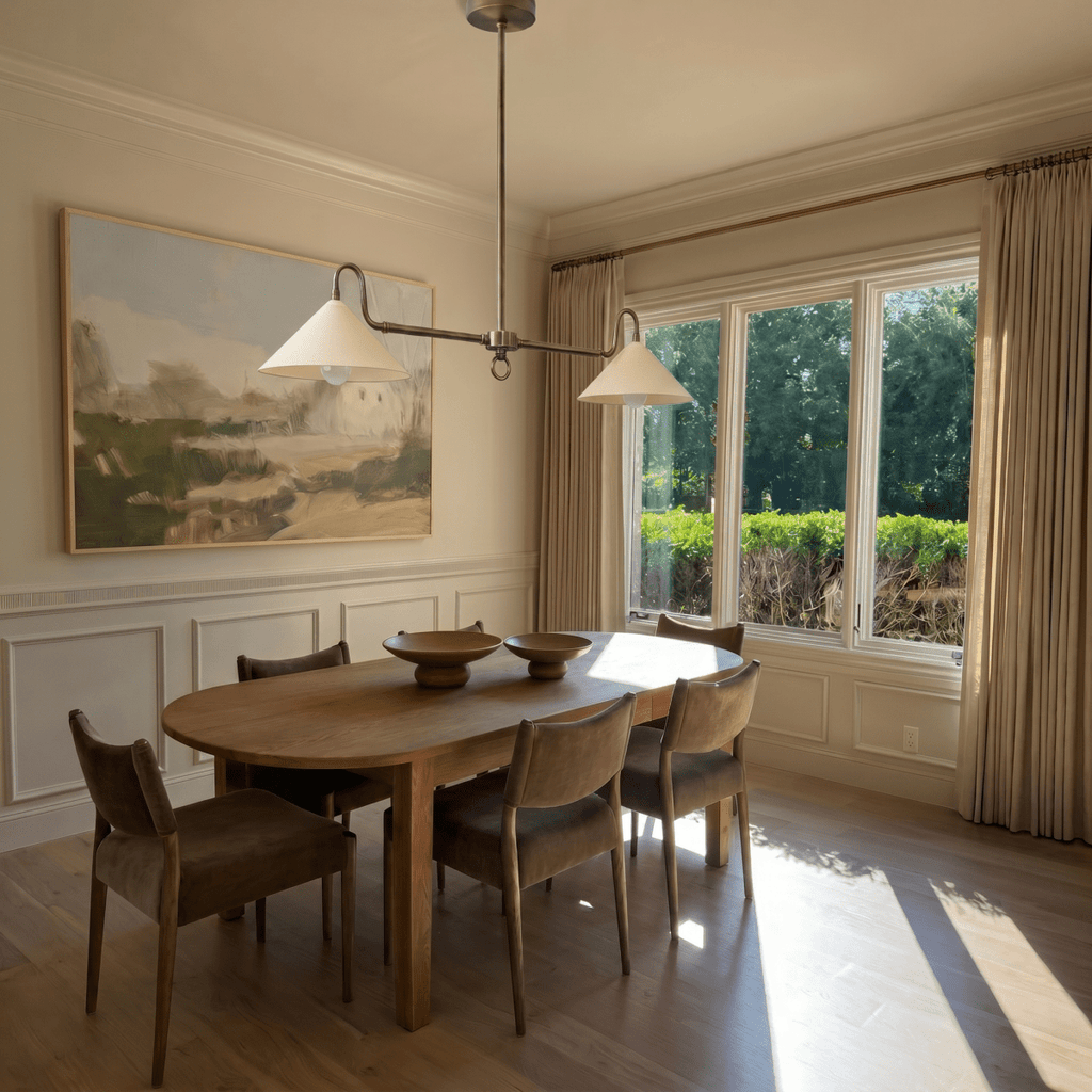This chrome Clérachic pendant light hangs above an oval dining table beneath a framed landscape painting.