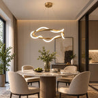 This Clérachic pendant hangs above a round marble dining table with cream chairs, its silicone ribbon glowing around a brass ring.