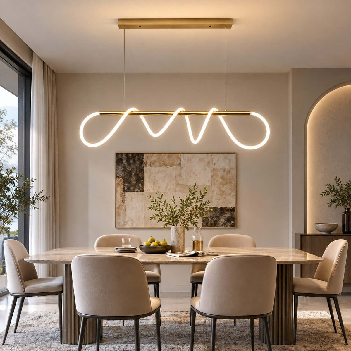 Brass bar pendant from Clérachic with a looping silicone ribbon lit white, above a dining table with taupe chairs and an arched alcove.