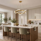 Round Clérachic pendant with a glowing silicone wave over a kitchen island with sage-green stools and white cabinets behind.