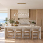Linear Clérachic pendant with a glowing silicone wave above a marble kitchen island with rattan stools and pale oak cabinets.