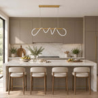 A long Clérachic pendant with a looped silicone ribbon above a marble island with cream stools, in front of taupe kitchen cabinets.