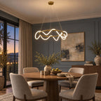 A Clérachic ring pendant with a lit silicone wave over a round walnut dining table with taupe chairs, in a blue-grey room at dusk.