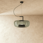 Clérachic glass pendant in smoky grey, wide rounded shade on a black curved arm and cord, over a limewash plaster wall.