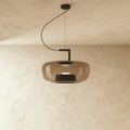 Clérachic wide pendant in amber glass with a black metal arm and cord, glowing softly against warm limewash plaster.