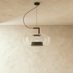 Clérachic wide pendant in pale grey glass on a black arm and cord, a black reflector cone inside, lit against plaster.