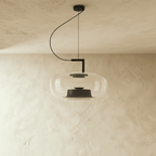 Clérachic pendant in pale grey glass, wide rounded shade with a black inner cone, unlit, hung from a black curved arm.