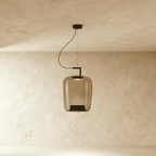 Clérachic tall pendant in amber glass, elongated shade with a black base cone, lit on a black curved arm.