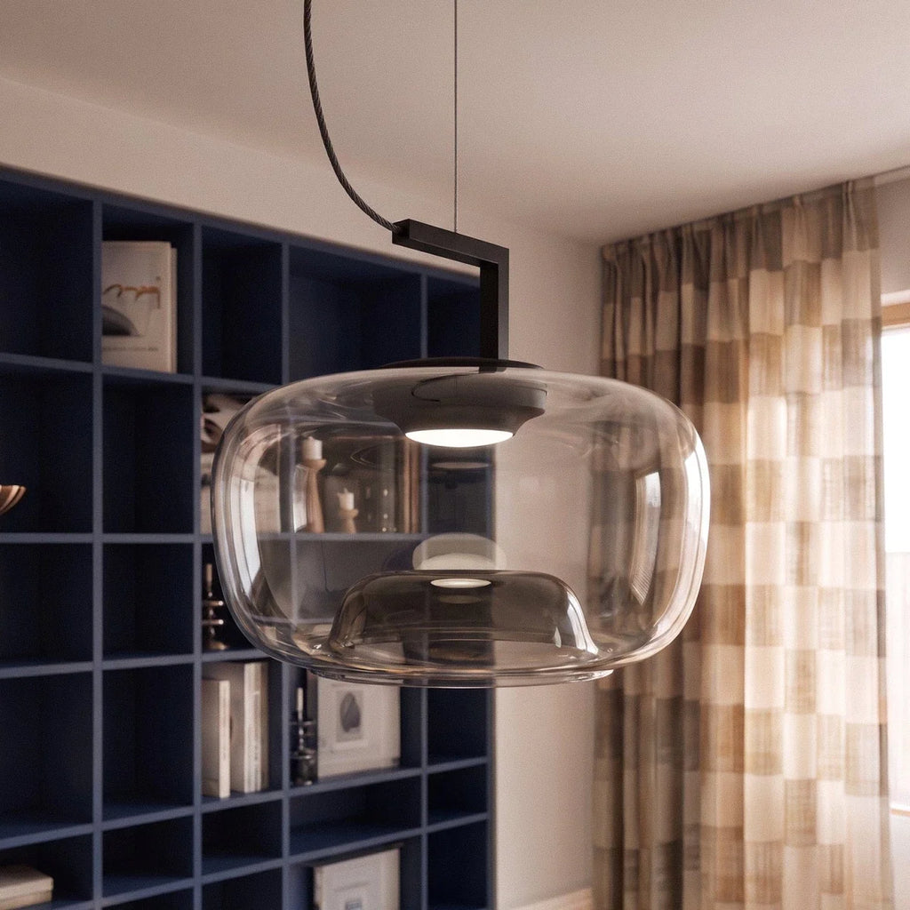Close view of a Clérachic wide glass pendant with a lit black reflector, beside navy shelves and checked curtains.