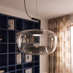 Close view of a Clérachic wide glass pendant with a lit black reflector, beside navy shelves and checked curtains.
