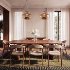 Two Clérachic amber glass pendants hung above a long walnut dining table with white lilies and sheer curtains.