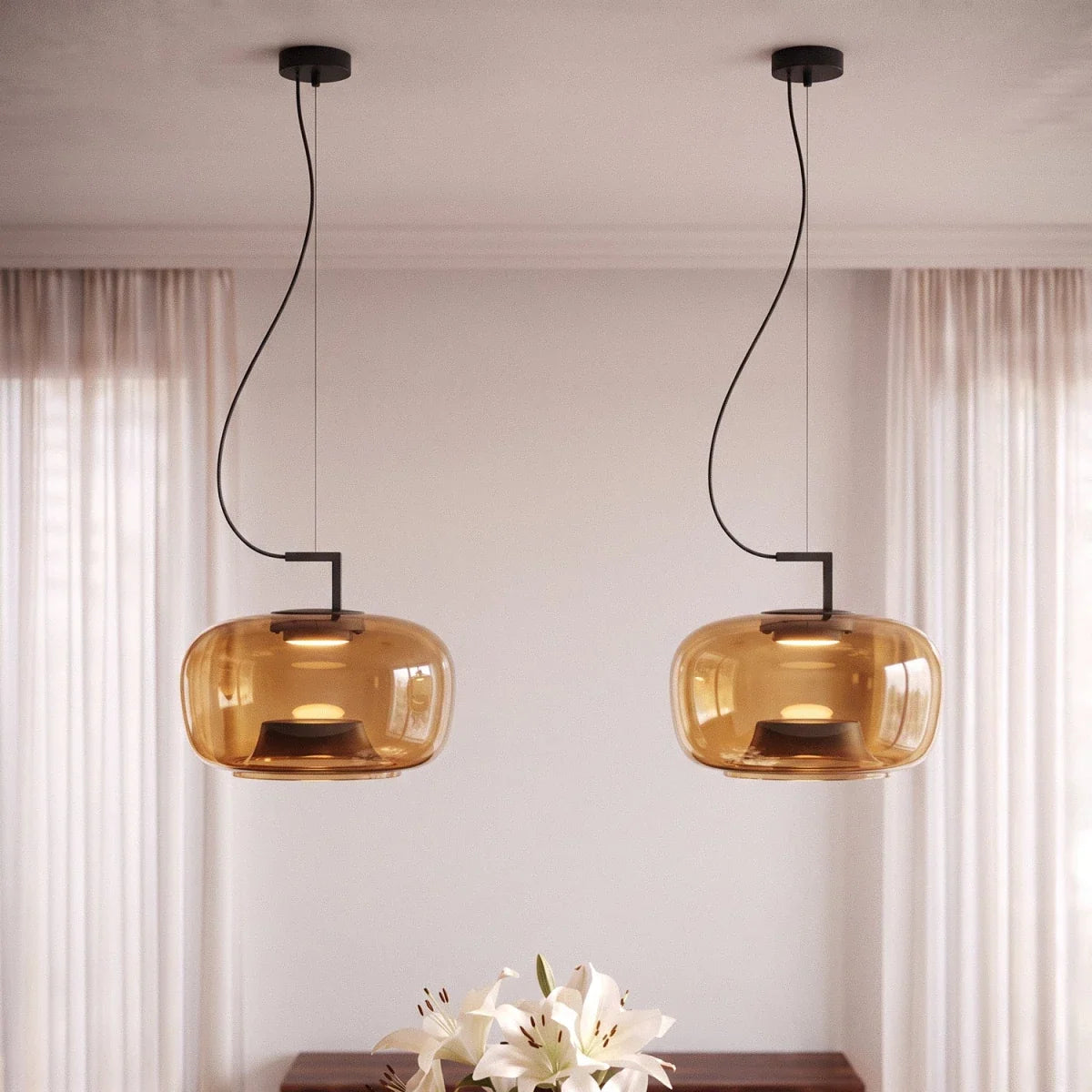 Clérachic pair of amber glass pendants lit warmly beside sheer curtains, with white lilies below.