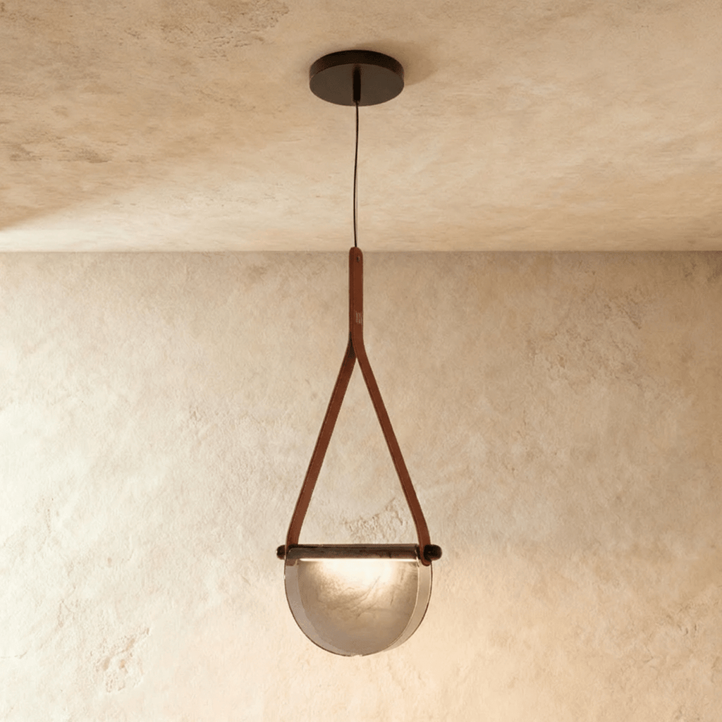 Clérachic pendant light with a tan leather strap holding a half-round smoked glass shade, hung from a dark ceiling canopy.