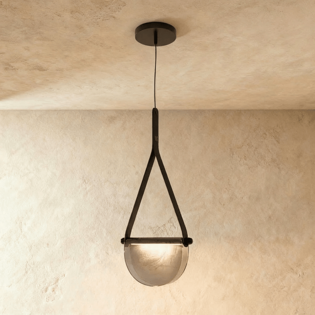 Clérachic pendant light with a black leather strap holding a half-round smoked glass shade, hung from a dark ceiling canopy.