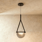 Clérachic pendant light with a black leather strap holding a half-round smoked glass shade, hung from a dark ceiling canopy.