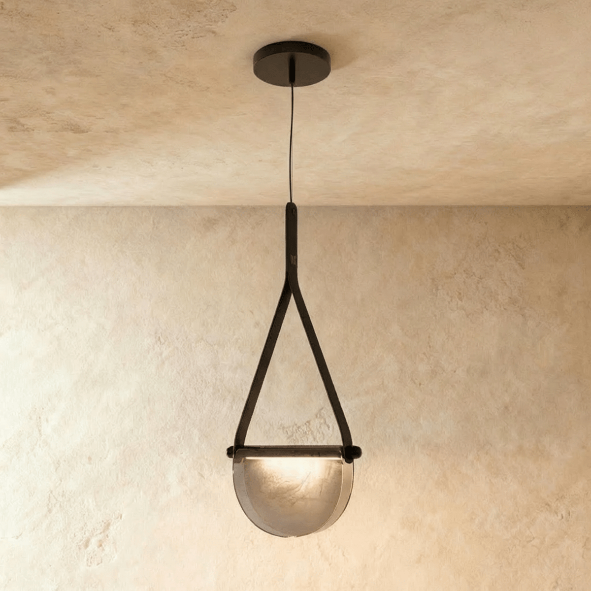 Clérachic pendant light with a black leather strap holding a half-round smoked glass shade, hung from a dark ceiling canopy.