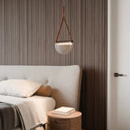 Clérachic pendant with a tan leather strap and half-round frosted glass shade hanging beside a bed against fluted walnut panelling.