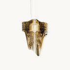 A Clérachic gold pendant of layered acrylic fins falling in a fluid, sculptural shape, on a plain off-white backdrop.