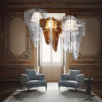 Three fringe pendants, one in a warm copper-gold and two clear, hang before a tall window above two grey armchairs, a Clérachic cluster.