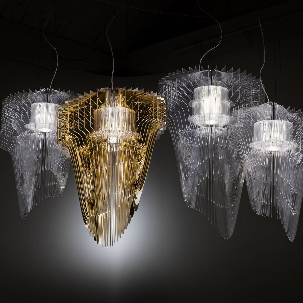 A gold fringe pendant glows between clear ones in a dark room, a Clérachic cluster with soft light spilling onto the floor below.