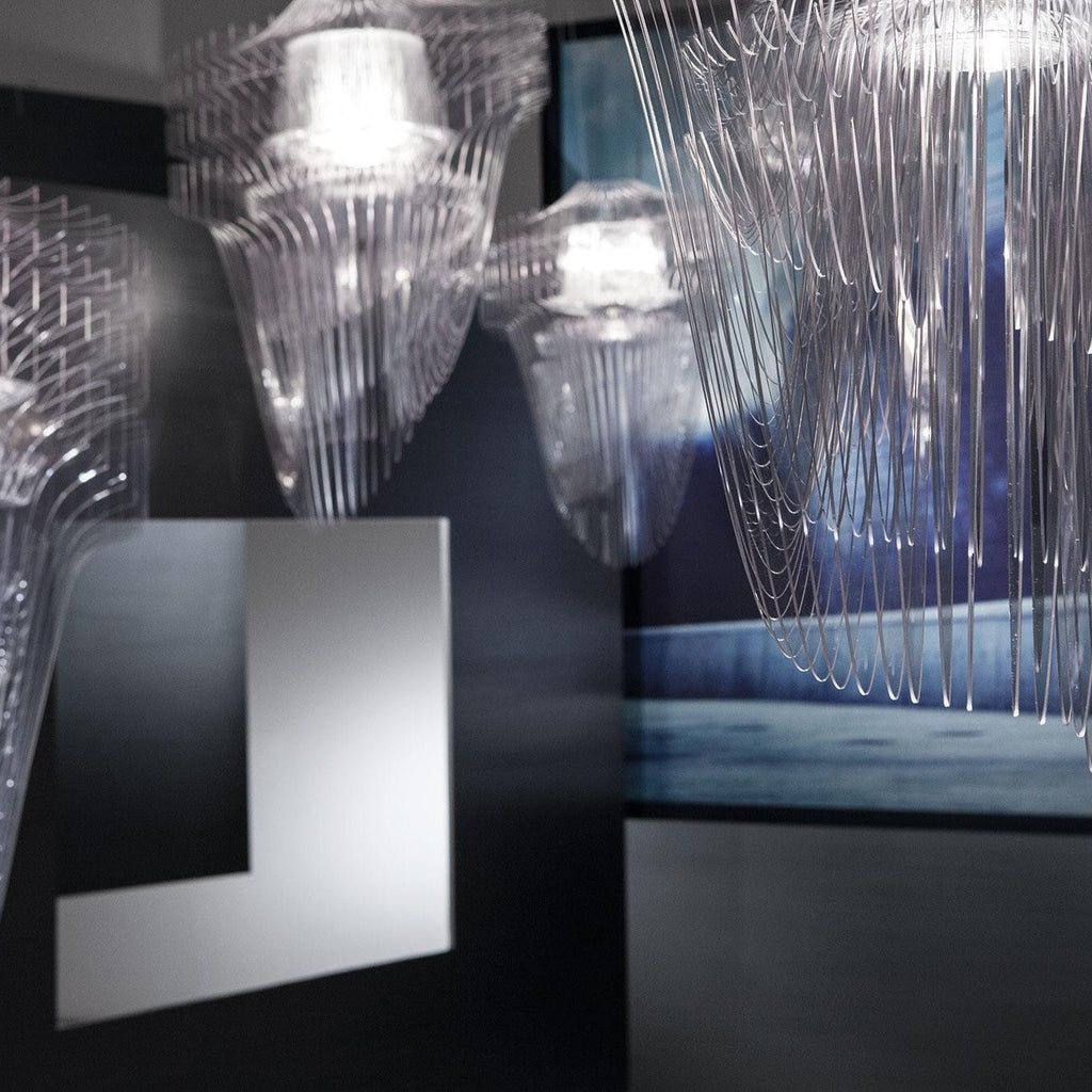 Close view of clear acrylic fringe pendants lit from within, shown in a dark gallery space from Clérachic.
