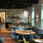 In a restaurant with a bar behind, a clear acrylic fringe pendant from Clérachic hangs over a long table laid with plates and glasses.