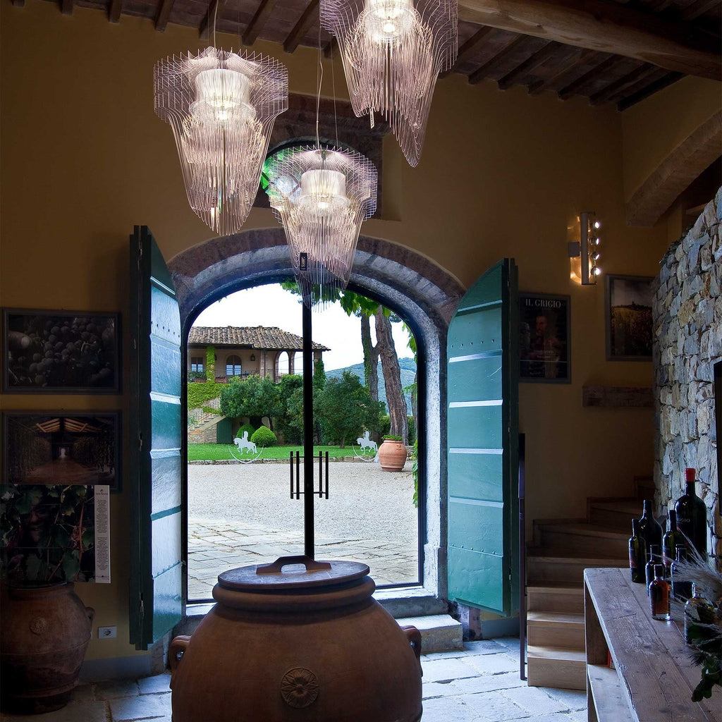 Several clear fringe pendants from Clérachic hang in a rustic hall with timber beams, in front of open green doors and a courtyard.