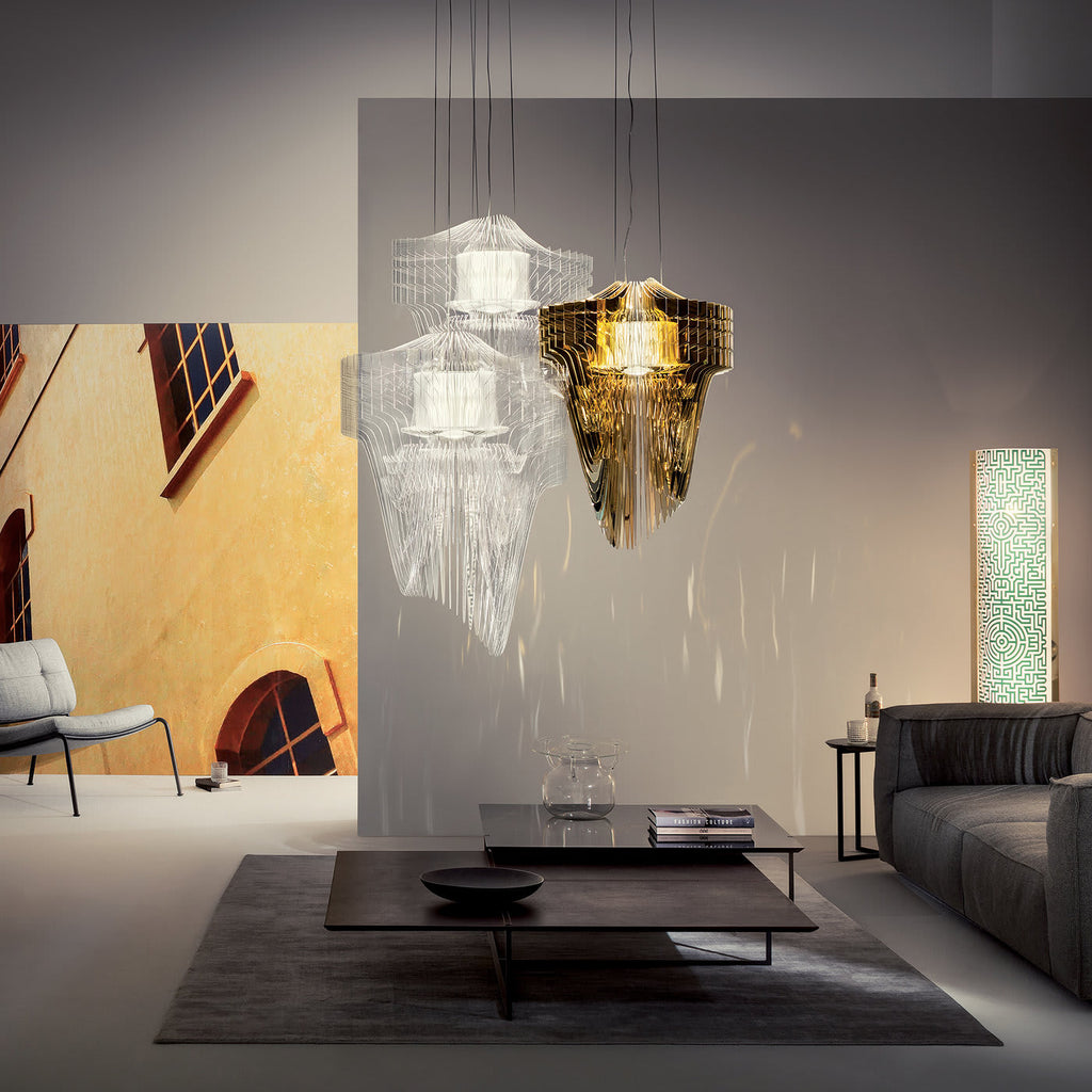 Clear and gold fringe pendants hang above a low dark coffee table and grey sofa in a bright living room from Clérachic.