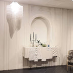 A pale, sculpted fringe light from Clérachic hangs at the top of the frame in a white room with an arched niche and a carved white sideboard.
