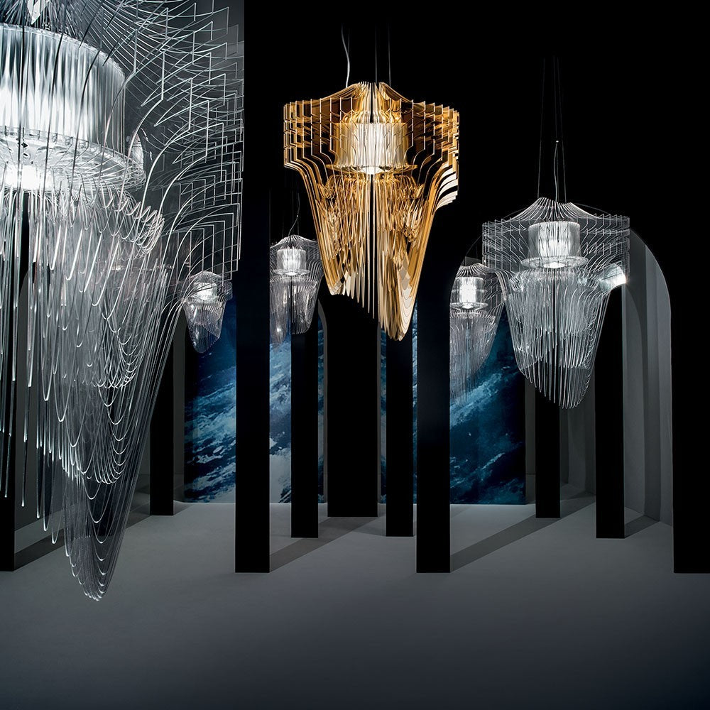 A gold pendant stands out among clear ones in a dark room with tall black columns, a Clérachic fringe cluster in a gallery.