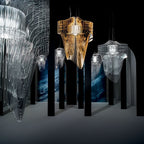 A gold pendant stands out among clear ones in a dark room with tall black columns, a Clérachic fringe cluster in a gallery.