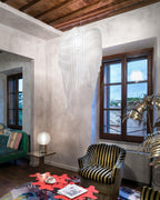 A clear acrylic fringe pendant from Clérachic hangs in a corner of a room with a beamed ceiling, a striped armchair and a red coffee table.