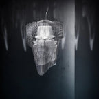 A clear acrylic fringe pendant from Clérachic, lit from within, hangs against a dark wall with soft shadows behind it.
