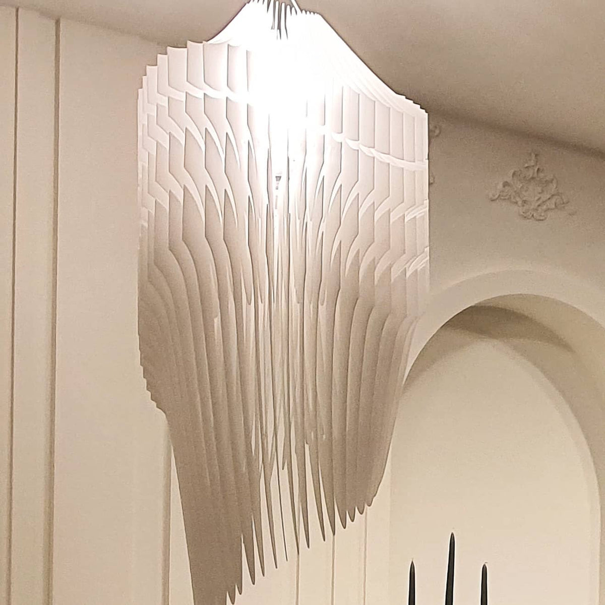 Close view of the layered ivory fins of a fringe pendant, lit warm from inside and framed by a plastered archway at Clérachic.