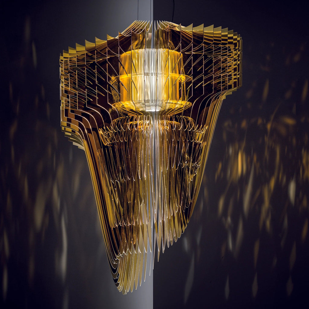A gold fringe pendant from Clérachic glows warm amber against a dark blue background, with the stacked fins reflecting like mirrors.