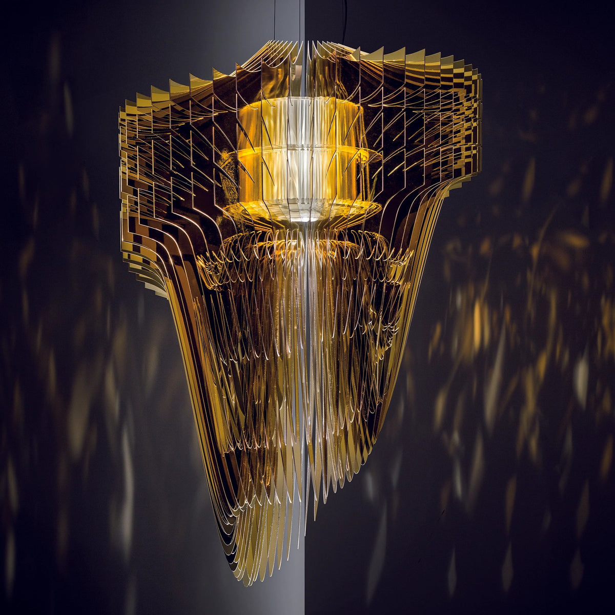 A gold fringe pendant from Clérachic glows warm amber against a dark blue background, with the stacked fins reflecting like mirrors.