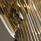 Close view of the curved gold fins on a Clérachic pendant, shown with soft focus and warm reflections between the plates.