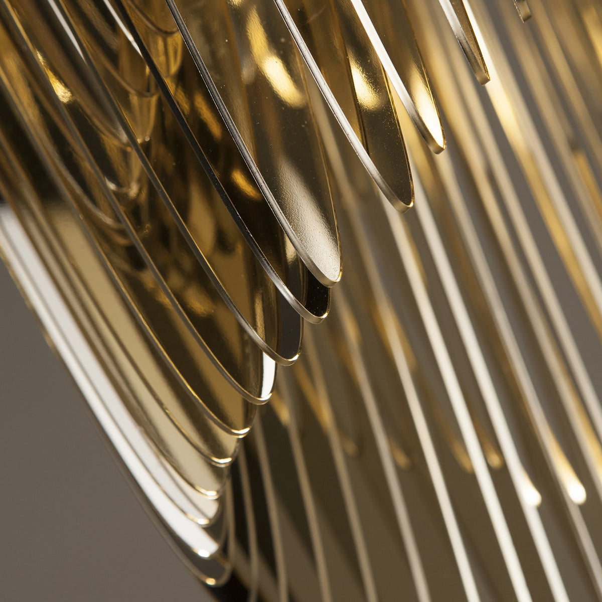 Close view of the curved gold fins on a Clérachic pendant, shown with soft focus and warm reflections between the plates.