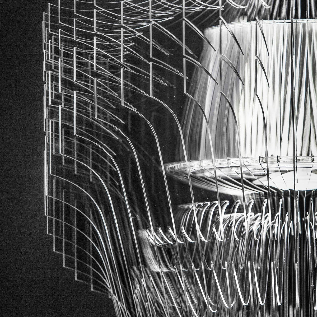 Close view of clear acrylic fins and the inner shade of a Clérachic fringe pendant, in black and white against a dark ground.