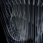 Close view of clear acrylic fins hanging in long, fine curves on a Clérachic pendant, shown against a dark backdrop.