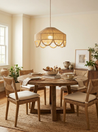 In a dining room with a round wood table and rattan chairs, this Clérachic pendant hangs lit above a jute rug.