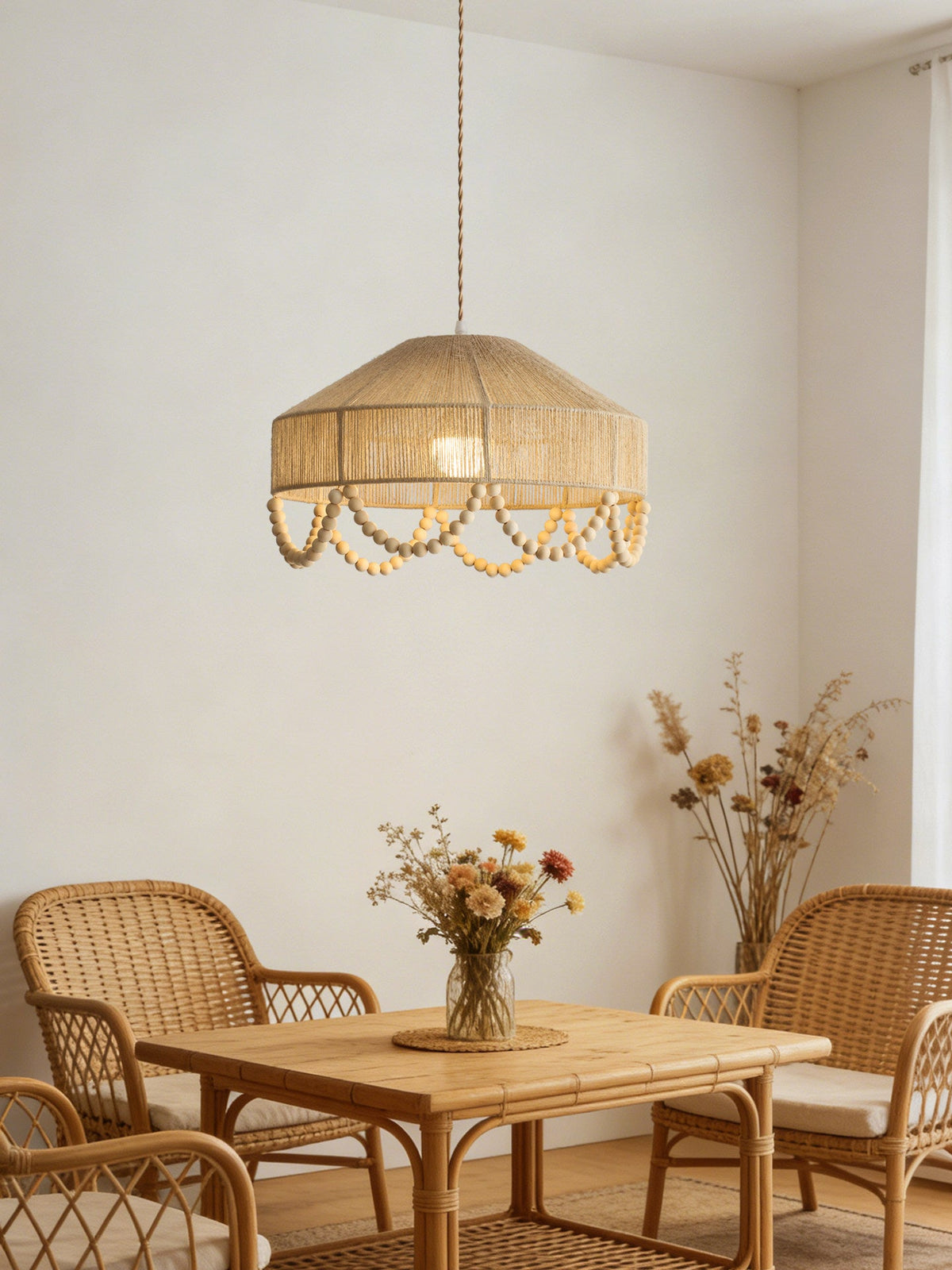 Over a small rattan breakfast table set with dried flowers, this Clérachic pendant glows in a plain white nook.