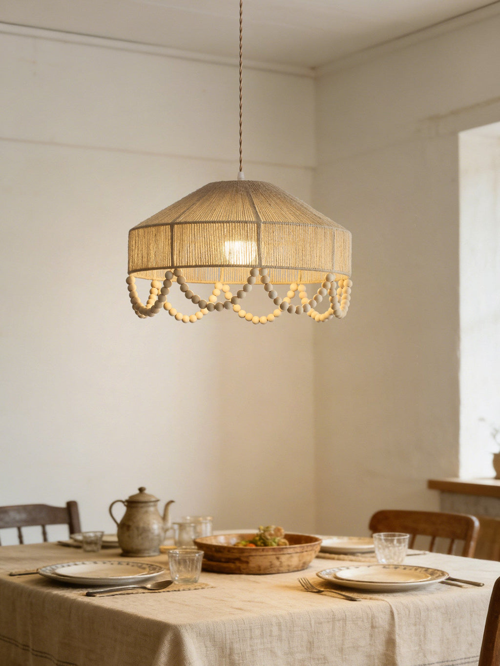 Above a linen-set dining table with pottery and glassware, this Clérachic pendant glows warm.