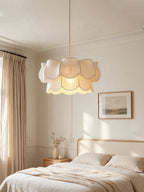 This Clérachic pendant, its linen petals layered in two tiers, hangs above a bed with panelled walls behind.