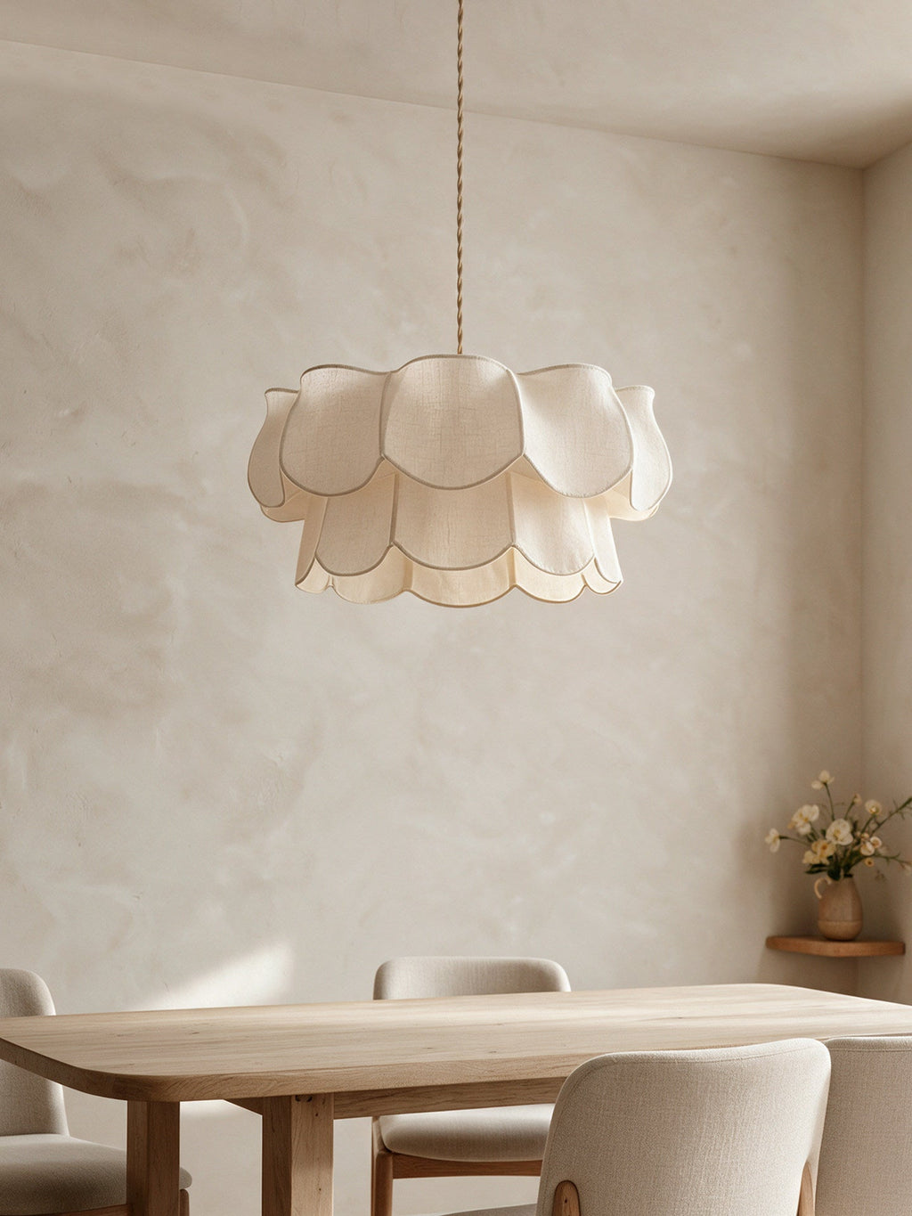 Layered linen petals on this Clérachic pendant hang above a wooden dining table set against a plastered wall.