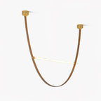 Two brass canopy plates and a single curved leather strap loop holding one glowing LED bar, on this Clérachic pendant against a white backdrop.