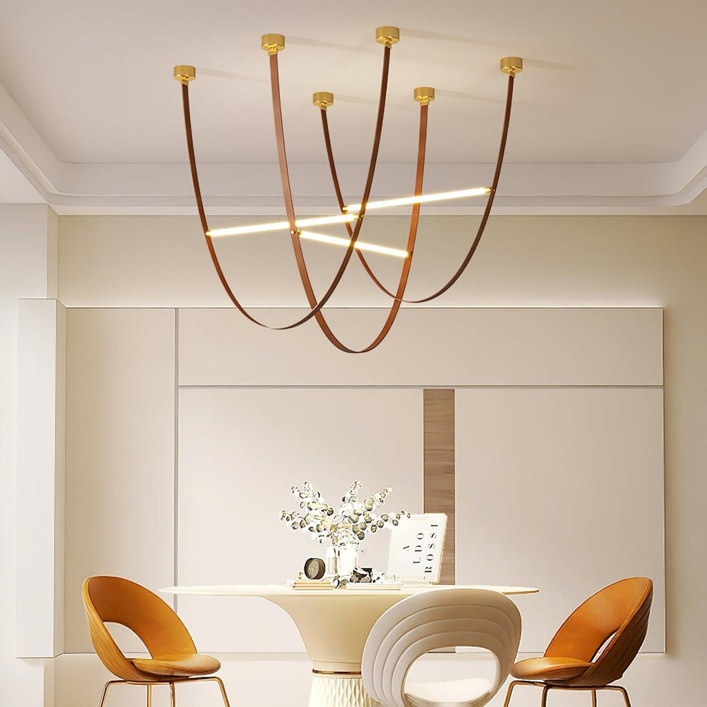 A cluster of this Clérachic pendant's leather loops and light bars hanging above a round dining table with two tan chairs.