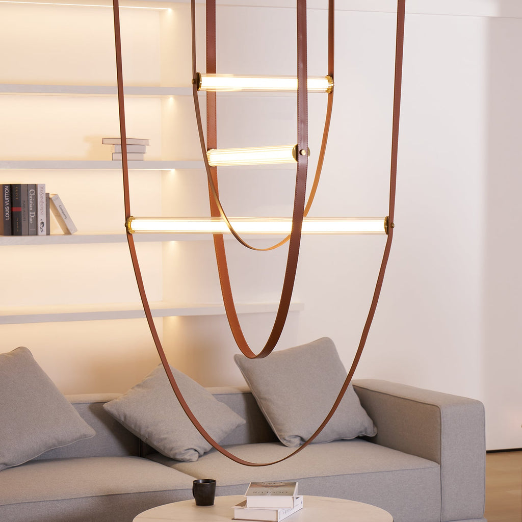 Close, low view of this Clérachic pendant's leather loops and three lit bars above a grey sofa and shelves lit from within.