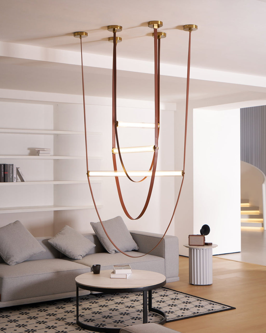 Six brass canopy plates on the ceiling feed this Clérachic pendant's leather loops down towards a sofa and a round coffee table.
