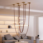Warm light bars on this Clérachic pendant glow in front of backlit white shelves, with a grey sofa below.